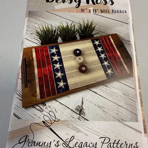 May include: A Betsy Ross 10" x 19" wool runner with a patriotic design. The runner features red and white stripes, blue star accents, and three game pieces. The design is inspired by Granny's Legacy Patterns.