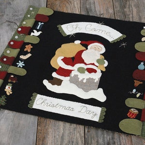 May include: A black felt Christmas stocking with a green and red border. The stocking features an applique of Santa Claus carrying a bag of gifts. The text "Oh Come... Christmas Day" is embroidered on the stocking.