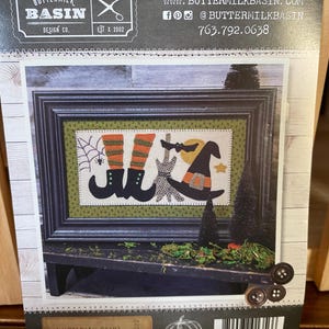 May include: A black and white illustration of a witch with a black cat and a pair of boots. The illustration is framed in a black frame and is on a wooden surface. The text "Matilda's Gear" and "Size: 7 x 12" is printed on the bottom of the image. The text "BD-1672" is printed on the right side of the image.