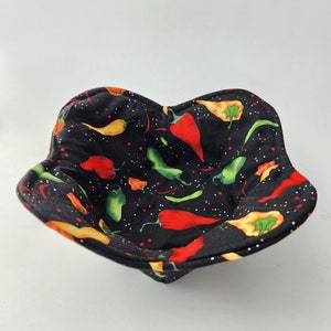 May include: A black fabric bowl with a chili pepper pattern. The bowl is filled with red, green, and yellow chili peppers on a black background with white dots.