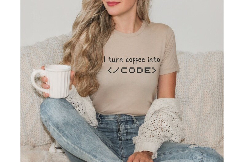 May include: A woman wearing a beige t-shirt with the text "I turn coffee into <CODE>" printed on it. She is holding a white mug and sitting on a white couch.