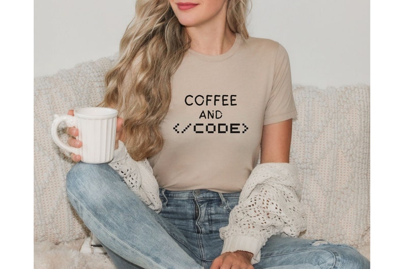 May include: A woman wearing a beige t-shirt with the text "COFFEE AND <CODE>" printed on it. She is sitting on a white couch and holding a white mug.