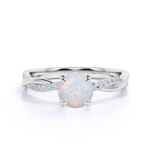 May include: A white opal engagement ring with a twisted band set with small diamonds. The ring is made of white gold and has a delicate design.