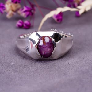 May include: A silver ring featuring a large, round, purple gemstone set in the centre. The ring has a wide band with a slightly rounded edge.