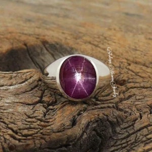 Peut inclure: Une bague en argent avec une grande pierre précieuse en rubis étoilé de forme ovale. Le rubis est de couleur rouge foncé avec un motif en forme d'étoile au centre.