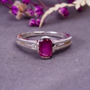 May include: A silver ring featuring a pink oval gemstone and two smaller white gemstones on either side. The ring is engraved with the text "Antique Heaven Jewelry".