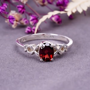 Pode incluir: Um anel de prata com uma gema vermelha e um design delicado. O anel é gravado com as palavras "Heirloom Heaven Jewelry".