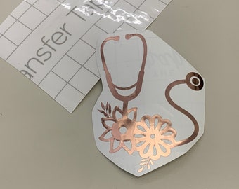 May include: A rose gold vinyl decal of a stethoscope with floral accents. The decal is on a white background.