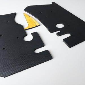May include: Three black foam pieces with cutouts, designed to fit together like a jigsaw. The pieces are likely for a car interior.