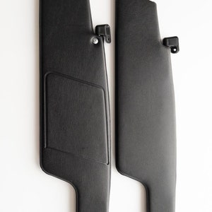 May include: A pair of black car sun visors with a textured surface. The visors have a simple design and are made of a durable material.