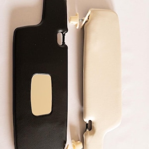 May include: Two car sun visors, one black and one beige, with a small rectangular mirror on the black visor.