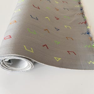 Puede incluir: Un rollo de tela gris con un patrón repetitivo de formas geométricas de colores, incluyendo cuadrados, triángulos y zigzags.