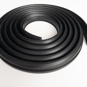 Könnte beinhalten: Eine aufgerollte Rolle schwarzer Gummi-Wetterleiste. Die Wetterleiste ist einfarbig schwarz und scheint neu zu sein. Der Gummi ist flexibel und hat ein abgerundetes Profil. Das Produkt dient zum Abdichten von Lücken.