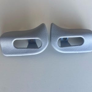 May include: Two gray plastic sun visor clips. The clips have a rectangular shape with a rounded edge and a small hole in the center.