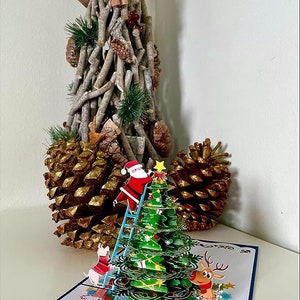 Carte pop-up 3D du Père Noël décorant un sapin de Noël. Une délicieuse carte de voeux surprise pour les enfants, les amis et la famille. 15 cm x 15 cm image 2