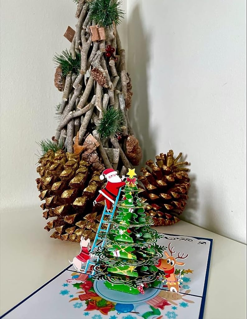 Carte pop-up 3D du Père Noël décorant un sapin de Noël. Une délicieuse carte de voeux surprise pour les enfants, les amis et la famille. 15 cm x 15 cm image 2