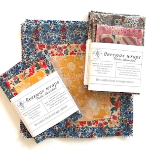 May include: A selection of reusable beeswax wraps with floral designs. The wraps, in various sizes, display patterns of blue, red, yellow, and white flowers. Made from natural beeswax, pine tree resin, organic almond oil, and 100% cotton, these wraps offer a plastic alternative.