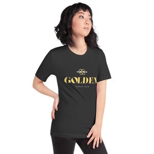 May include: Black t-shirt featuring the word "GOLDEN" in gold lettering. Above "GOLDEN" is a gold infinity symbol and the word "HUXTRUX". Below "GOLDEN" is "WORLD TOUR". The t-shirt is worn by a person.