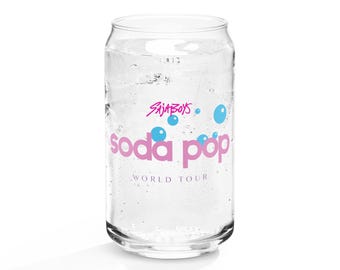 May include: A clear glass soda can-shaped glass filled with ice and a clear liquid. The glass has the words "Saja Boys" and "soda pop" in pink, with blue bubble graphics. The words "WORLD TOUR" are below the "soda pop" text.