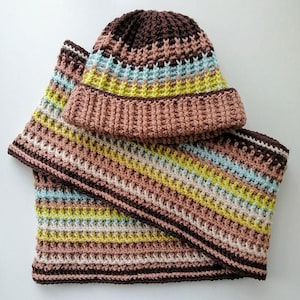 Peut inclure: Ensemble bonnet et écharpe crocheté à la main. Le bonnet est marron et rayé de rose, bleu et jaune. L'écharpe assortie présente les mêmes rayures et une bordure marron. L'ensemble est en fil doux.