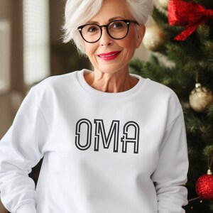 Peut inclure: Sweat-shirt blanc avec le mot "OMA" imprimé en lettres noires soulignées.