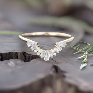 May include: A gold ring with a delicate, curved design featuring a row of small, clear baguette-shaped diamonds.