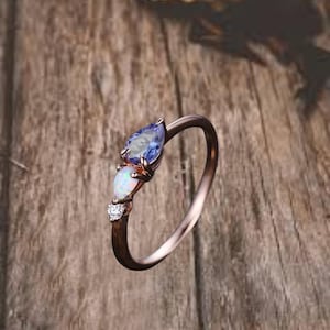 May include: A delicate rose gold ring with a pear-shaped opal and a pear-shaped blue gemstone. The ring is set with small sparkling diamonds.