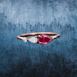 May include: A rose gold ring with a pear-shaped ruby gemstone, a pear-shaped opal gemstone, and a small round diamond gemstone.