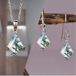 May include: A silver necklace and earrings set with a green and white agate stone pendant and matching earrings. The pendant and earrings are shaped like a square with rounded corners.