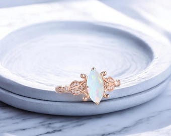 May include: A rose gold ring with a marquise-shaped opal gemstone surrounded by smaller clear gemstones. The ring has a delicate floral design.