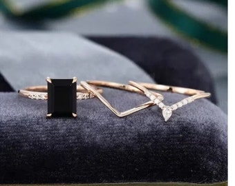 May include: A set of three gold rings with black and white diamonds. The center ring features a large, square-shaped black diamond. The other two rings are delicate and feature small white diamonds.