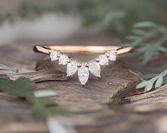 May include: A delicate rose gold wedding band with a curved design featuring a row of marquise-shaped diamonds.