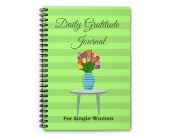 May include: A spiral-bound journal with a green striped cover. The cover features the text "Daily Gratitude Journal" and "For Single Women". A vase of colorful tulips sits on a small table. The journal's design is simple and elegant.