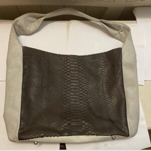 May include: A large, off-white leather tote bag with a brown snakeskin-patterned panel on the front.