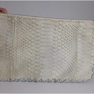 May include: A white snakeskin clutch purse with a zipper closure and a decorative stitch detail around the edges.