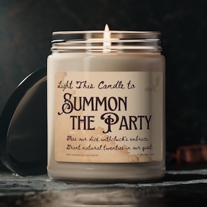 May include: A white candle in a glass jar with a brown label that reads "Light This Candle to SUMMON THE PARTY Bless our dice with luck's embrace, Grant natural twenties in our guest. 100% natural soy wax blend 100% cotton wick"