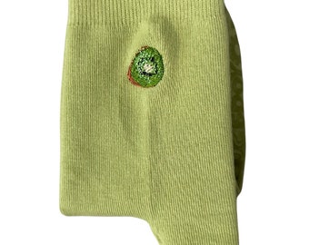 May include: Green cotton socks with a kiwi fruit embroidered on the front. The socks have a ruffled top.