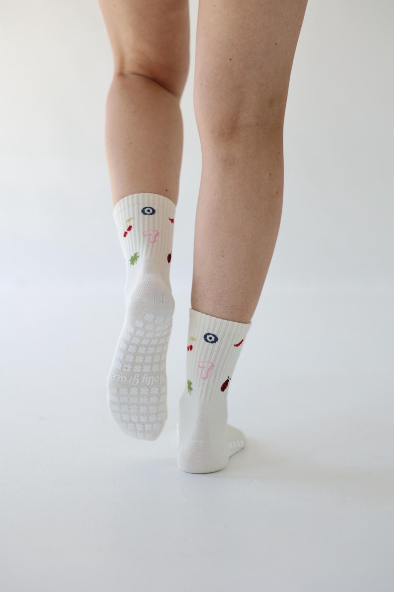 May include: Cream-coloured socks featuring embroidered patterns of a blue eye, red chilli, and a pink mushroom. The soles have a non-slip grip. These socks are a comfortable, everyday accessory.