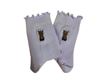 May include: A pair of lavender socks with a small embroidered Yorkshire Terrier on each sock. The socks have a frilly edge.