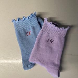 May include: Two pairs of socks with frilly tops. One pair is light blue with the initials "CC" embroidered on them. The other pair is lavender with the initials "MP" embroidered on them.