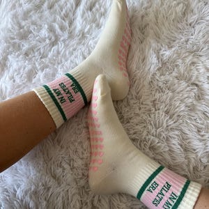 May include: Pair of white socks with pink hearts and green stripes. The socks have the text "IN MY ERA PILATES" on the side.