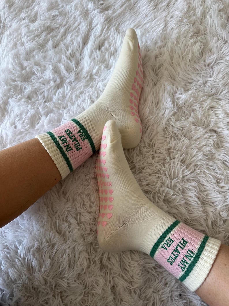 May include: Pair of white socks with pink hearts and green stripes. The socks have the text "IN MY ERA PILATES" on the side.