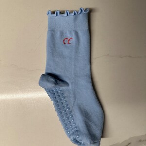 May include: Light blue socks with a frilled top and a red embroidered "CC" on the front. The socks have a grippy bottom with small dots.