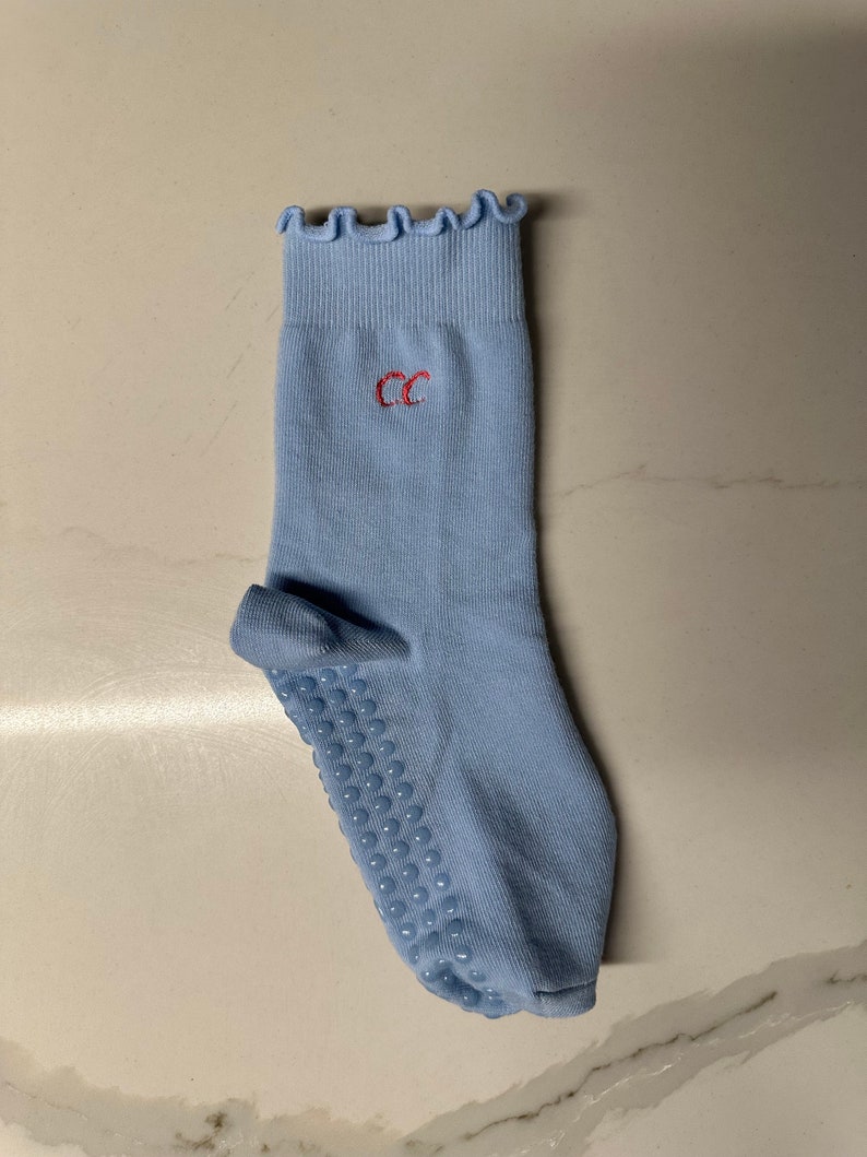 May include: Light blue socks with a frilled top and a red embroidered "CC" on the front. The socks have a grippy bottom with small dots.