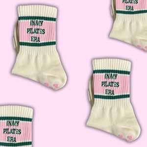 May include: White socks with pink and green stripes. The socks have the text "In My Pilates Era" embroidered on them.