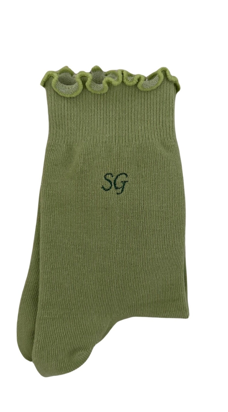 May include: Green ankle socks with a frilled top and the letters "SG" embroidered on the front.