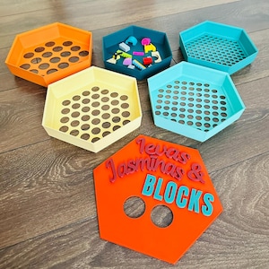 May include: A set of colorful, hexagonal storage trays in orange, teal, yellow, and blue. Some trays have perforated bottoms. An orange sign with the text "Texas Jasminas & BLOCKS" is also present.