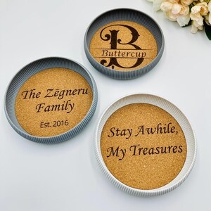 May include: Three round coasters with cork centres and textured rims. One coaster features the word "Buttercup" with a decorative "B", another says "The Zegneru Family, Est. 2016", and the third says "Stay Awhile, My Treasures".