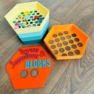 May include: Hexagonal toy storage containers in yellow, blue, and orange. One container is filled with colorful toys. An orange container has circular holes. An orange sign reads "Texas Jasminas & BLOCKS".