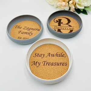 May include: Three round coasters with cork centres and grey or white ribbed edges. The coasters feature engraved text: "The Zegneru Family Est. 2016", "Buttercup", and "Stay Awhile, My Treasures".